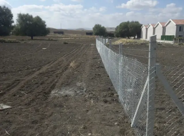 Sürülmüş tarla kenarında beton direkli tel örgü çit hattı